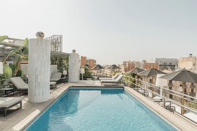 Pool on a roof with chairs, umbrellas, and buildings in the background 
