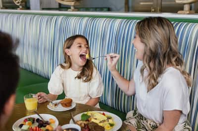 Smiling mother and young daughter enjoying a hearty breakfast with mother feeding her egg from fork 